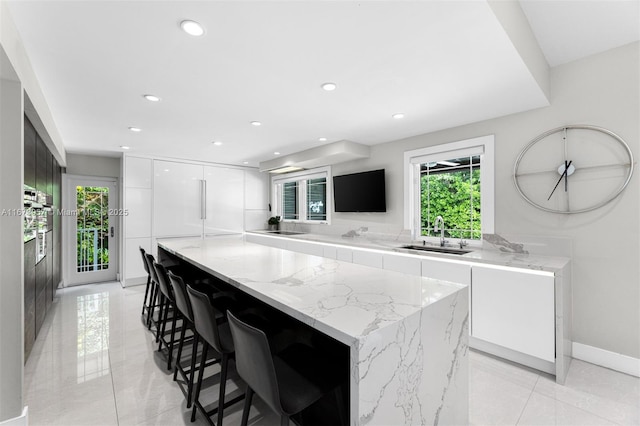 kitchen featuring sink, a breakfast bar, a center island, light stone counters, and white cabinets