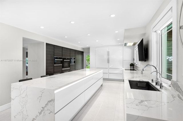 kitchen featuring sink, white cabinetry, a center island, light stone counters, and stainless steel oven