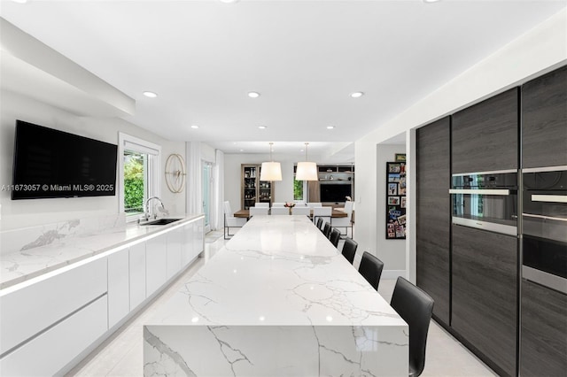 kitchen featuring a breakfast bar, sink, light stone counters, decorative light fixtures, and white cabinets