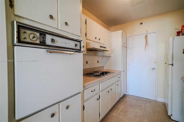 kitchen with white appliances, light tile patterned floors, light countertops, under cabinet range hood, and tasteful backsplash