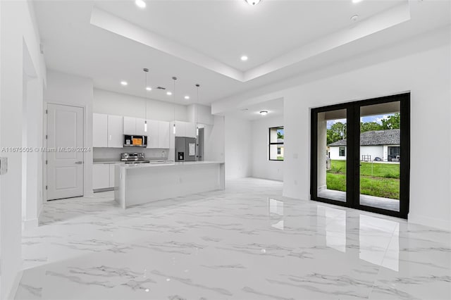 kitchen featuring a kitchen island with sink, pendant lighting, a raised ceiling, stainless steel appliances, and white cabinets