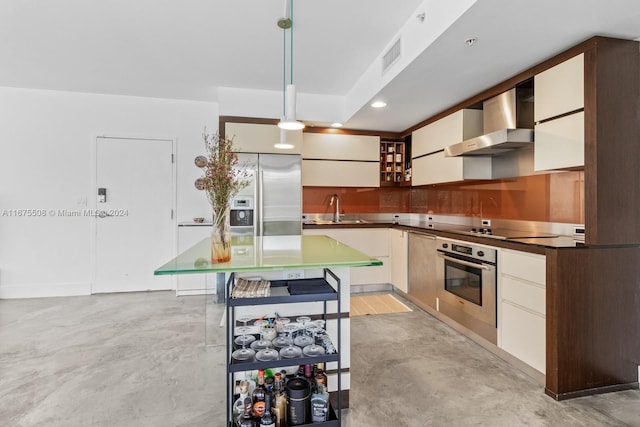 kitchen with sink, a kitchen island, decorative light fixtures, wall chimney range hood, and appliances with stainless steel finishes