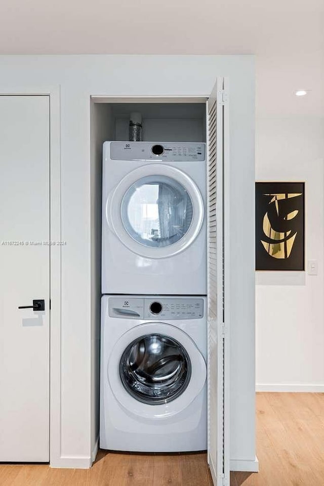 clothes washing area with stacked washer and dryer and light wood-type flooring