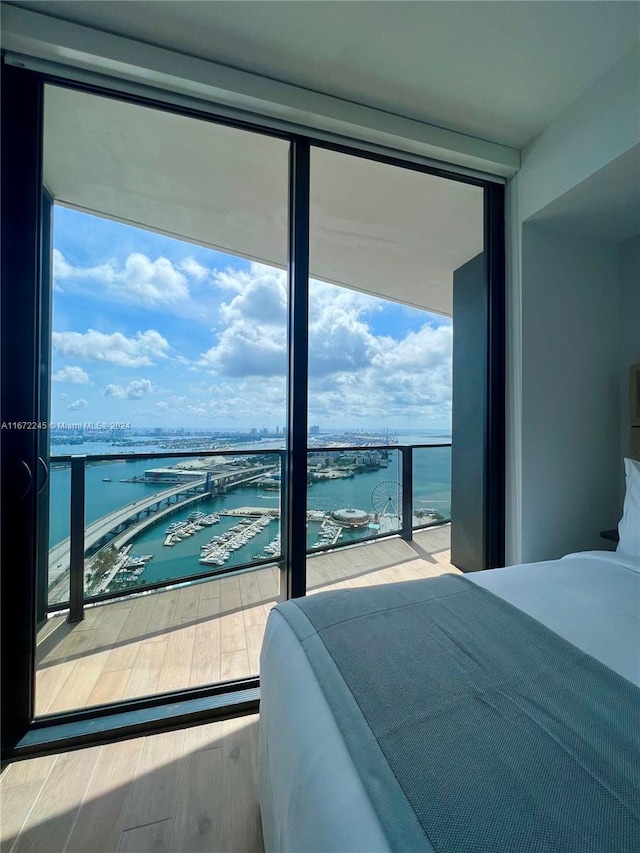 bedroom with a wall of windows, a water view, multiple windows, and hardwood / wood-style flooring