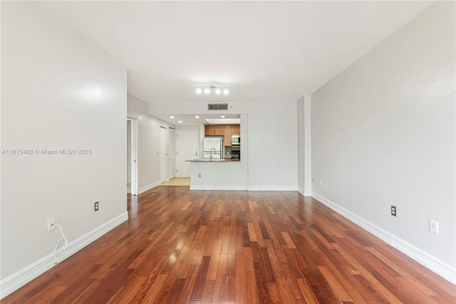 unfurnished living room with dark wood-style floors, visible vents, and baseboards