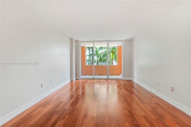 unfurnished room featuring baseboards, floor to ceiling windows, and wood finished floors