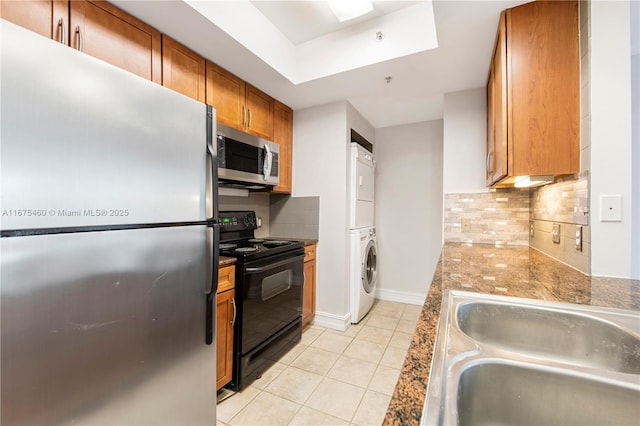 kitchen with brown cabinets, light tile patterned floors, stacked washer and dryer, appliances with stainless steel finishes, and a sink