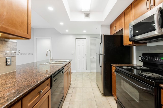 kitchen featuring a sink, visible vents, black appliances, brown cabinetry, and dark stone countertops