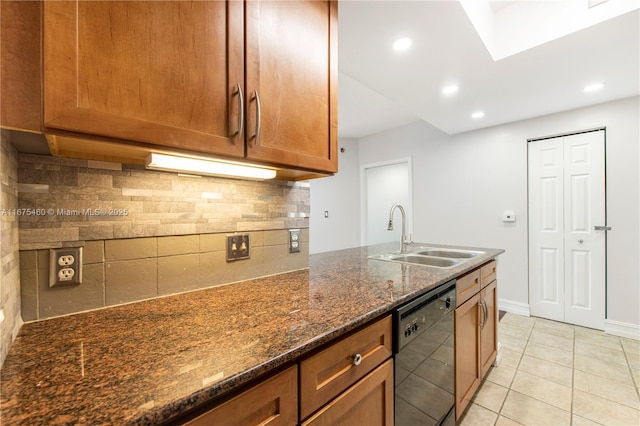 kitchen featuring light tile patterned floors, dishwasher, brown cabinets, dark stone countertops, and a sink