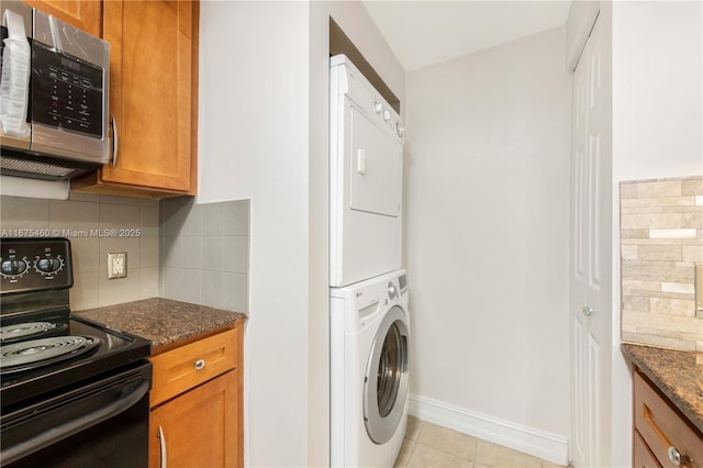 laundry area with light tile patterned floors, laundry area, baseboards, and stacked washer / drying machine