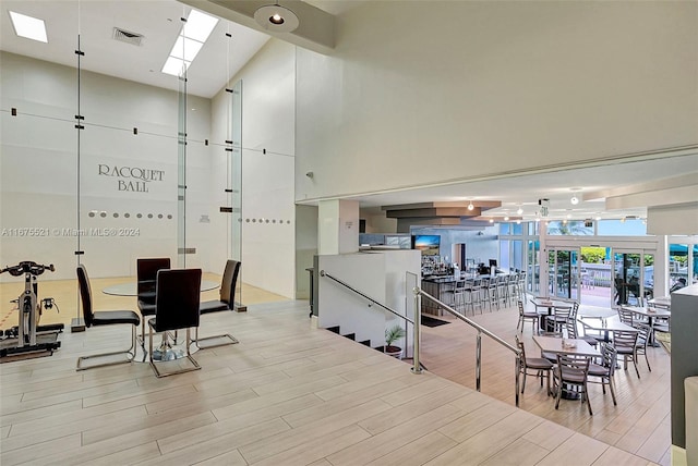 dining room featuring a towering ceiling, light hardwood / wood-style floors, and a skylight