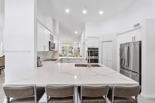 kitchen featuring light hardwood / wood-style flooring, decorative light fixtures, stainless steel appliances, kitchen peninsula, and white cabinetry