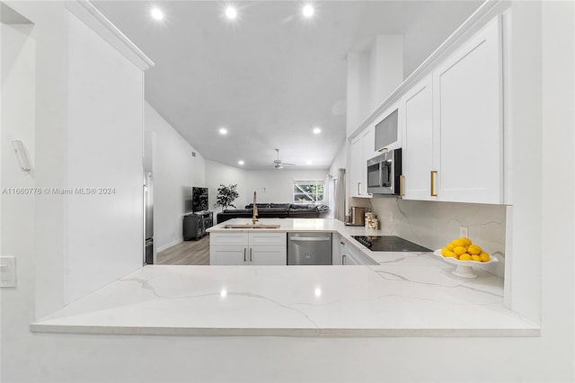 kitchen featuring stainless steel appliances, kitchen peninsula, light stone countertops, and white cabinetry