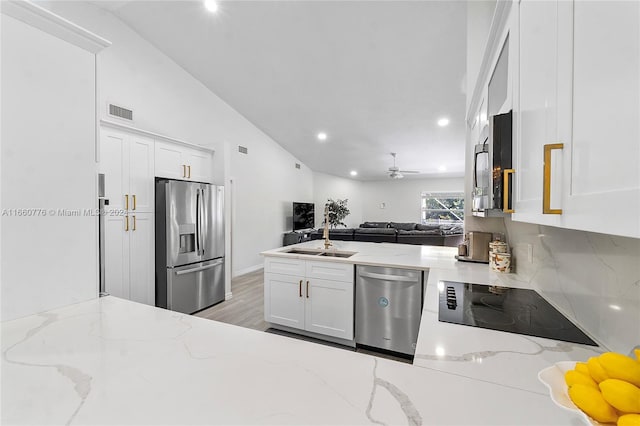 kitchen with white cabinets, lofted ceiling, sink, appliances with stainless steel finishes, and light stone countertops