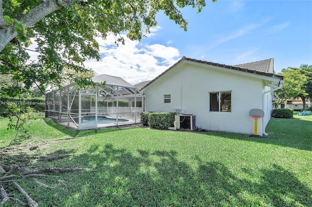 rear view of property with glass enclosure, central AC unit, and a lawn