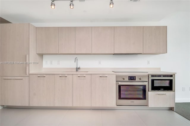 kitchen featuring light countertops, a sink, light brown cabinets, and stainless steel oven