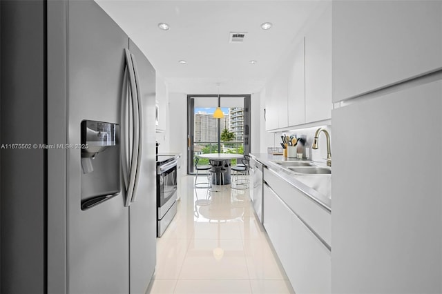 kitchen with light tile patterned flooring, sink, white cabinets, hanging light fixtures, and stainless steel appliances