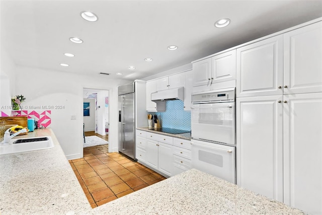 kitchen with white double oven, stainless steel built in fridge, white cabinetry, and sink