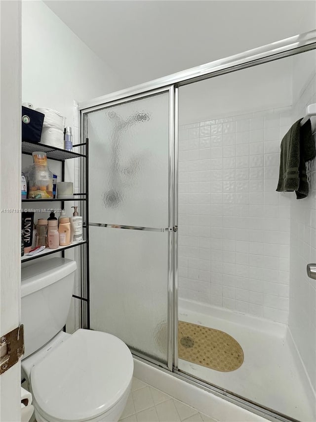 bathroom featuring tile patterned flooring, a shower with shower door, and toilet