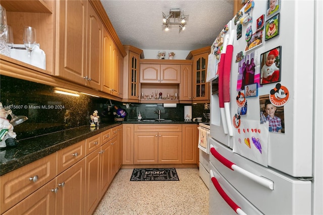 kitchen with a textured ceiling, dark stone countertops, sink, white refrigerator, and backsplash