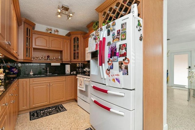 kitchen with tasteful backsplash, white appliances, dark stone counters, sink, and a textured ceiling