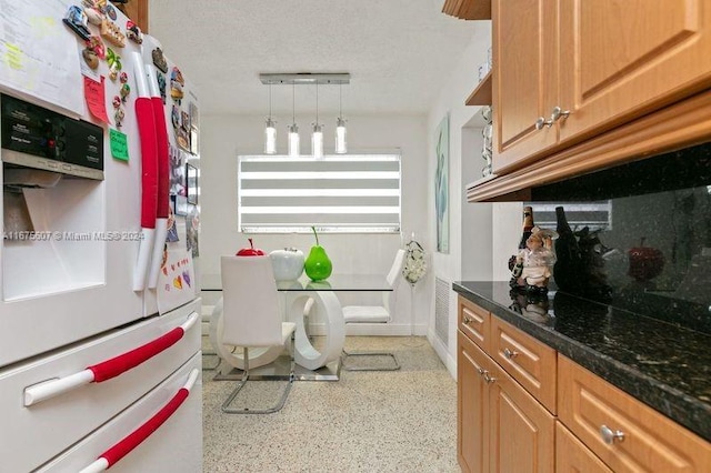 kitchen with dark stone counters, white fridge with ice dispenser, decorative light fixtures, and a textured ceiling