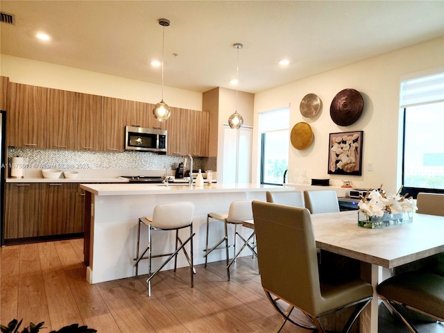 kitchen with a breakfast bar, pendant lighting, a kitchen island with sink, and tasteful backsplash