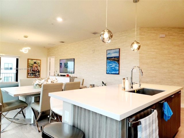 kitchen with a breakfast bar area, dishwashing machine, hanging light fixtures, and sink