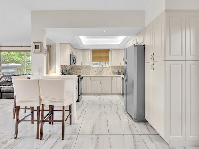 kitchen with stainless steel appliances, sink, tasteful backsplash, a breakfast bar area, and a tray ceiling