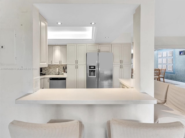 kitchen with white cabinets, kitchen peninsula, a breakfast bar area, tasteful backsplash, and appliances with stainless steel finishes