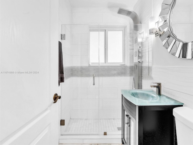 bathroom featuring a shower with door, vanity, toilet, and tile walls