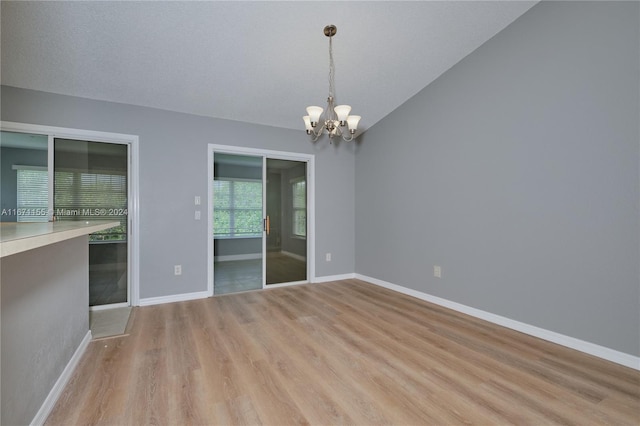 unfurnished room with vaulted ceiling, a textured ceiling, a notable chandelier, and light wood-type flooring