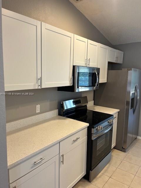 kitchen with white cabinetry, light tile patterned flooring, stainless steel appliances, and lofted ceiling