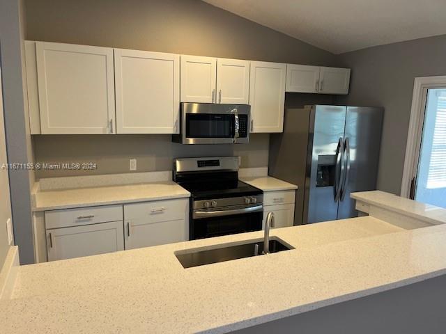 kitchen with lofted ceiling, sink, light stone countertops, white cabinetry, and stainless steel appliances