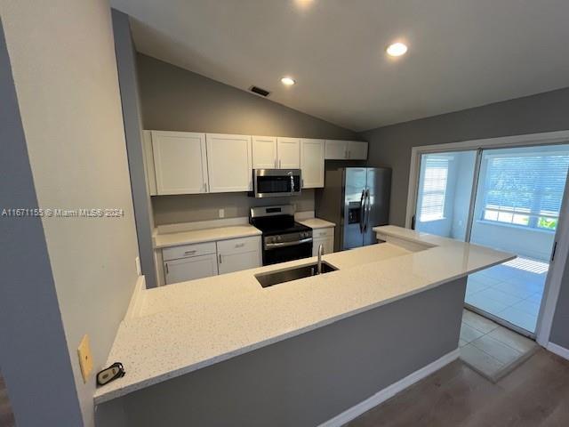 kitchen featuring white cabinets, sink, vaulted ceiling, light hardwood / wood-style floors, and stainless steel appliances