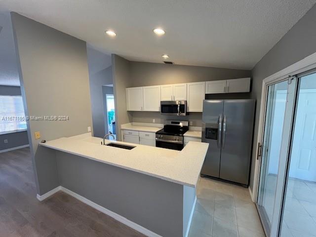 kitchen featuring white cabinetry, sink, stainless steel appliances, lofted ceiling, and light wood-type flooring