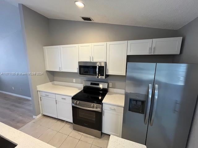 13592 Clara Ln, Port Charlotte, FL 33981 - kitchen with stainless steel appliances, lofted ceiling, light countertops, white cabinetry, and light tile patterned floors
