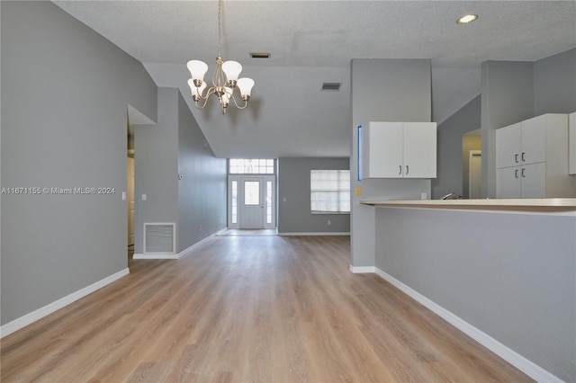 interior space featuring a chandelier, pendant lighting, a textured ceiling, light hardwood / wood-style floors, and white cabinets