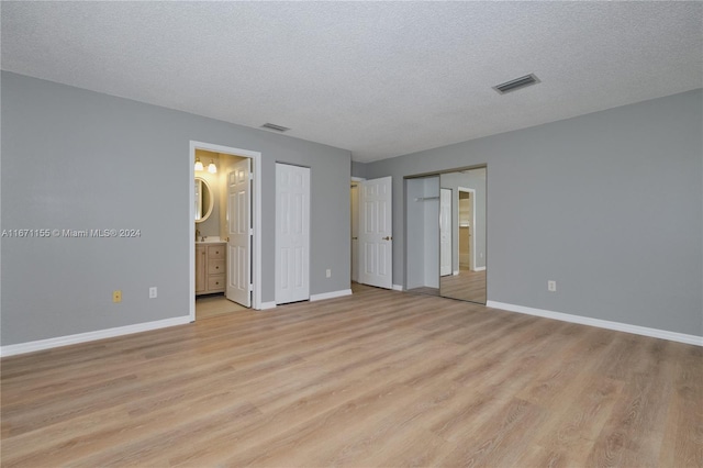 unfurnished bedroom featuring light wood-type flooring, a textured ceiling, and connected bathroom