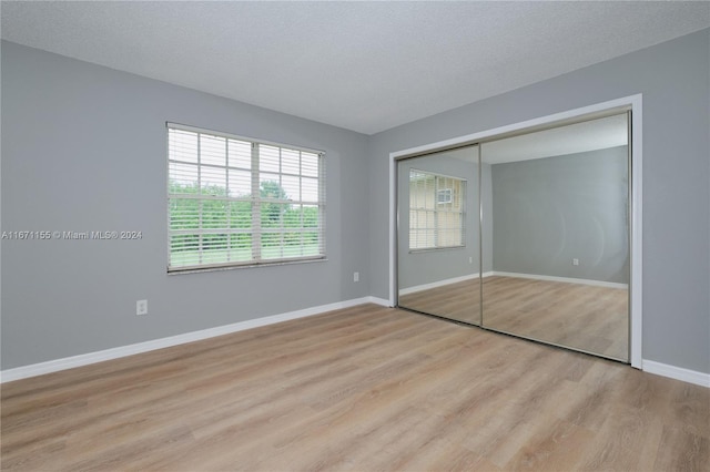 unfurnished bedroom with light wood-type flooring, a textured ceiling, and a closet