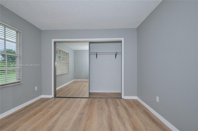 unfurnished bedroom with a textured ceiling, light wood-type flooring, and a closet