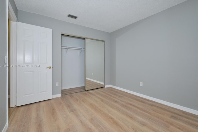 unfurnished bedroom with light wood-type flooring, a textured ceiling, and a closet