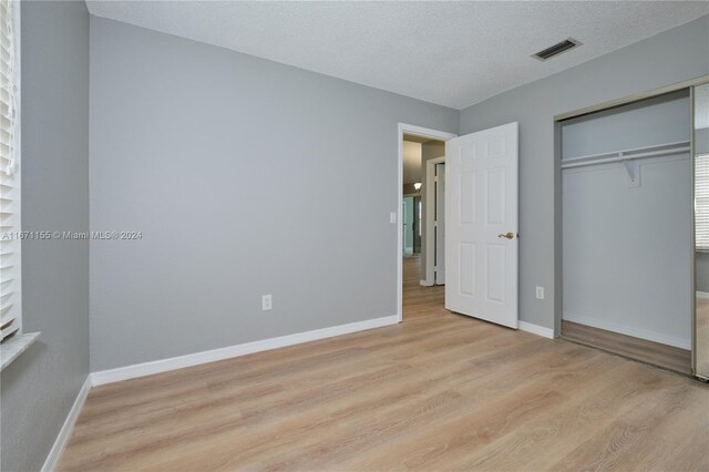 unfurnished bedroom with a closet, a textured ceiling, and light hardwood / wood-style flooring