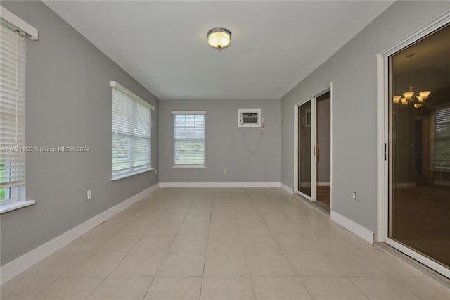 empty room featuring a wall unit AC, light tile patterned flooring, and a chandelier