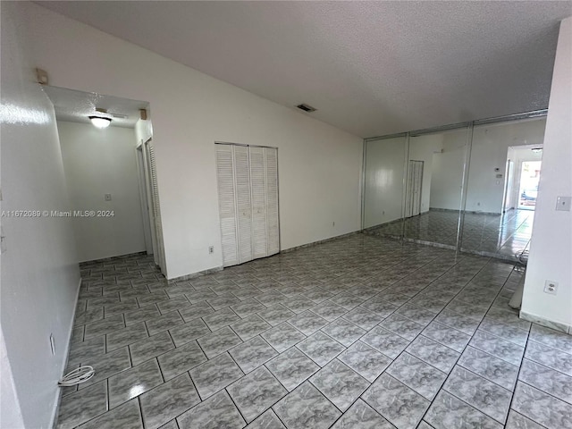 tiled spare room featuring a textured ceiling and vaulted ceiling