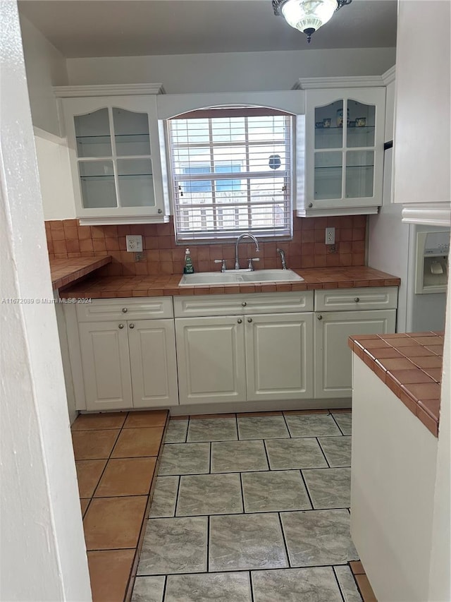 kitchen with tile counters, backsplash, sink, light tile patterned floors, and white cabinets