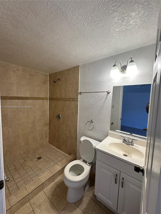 bathroom with a tile shower, a textured ceiling, toilet, vanity, and tile patterned flooring