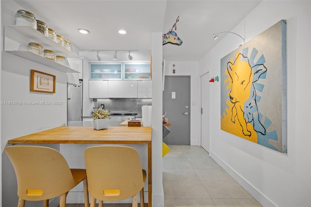 kitchen with white cabinets, tasteful backsplash, freestanding refrigerator, rail lighting, and light tile patterned floors
