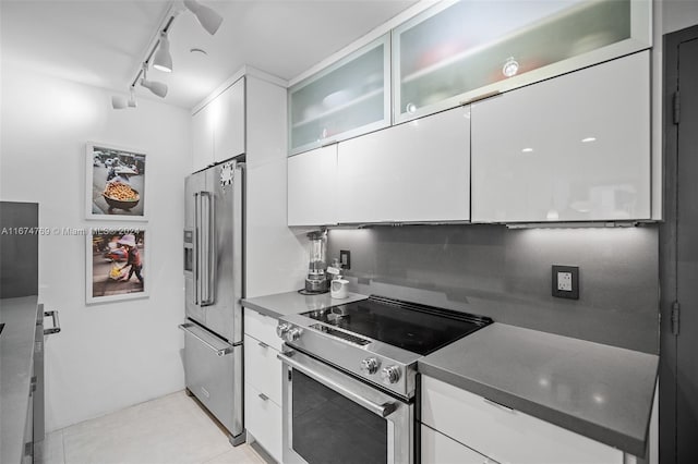 kitchen with dark countertops, white cabinetry, glass insert cabinets, rail lighting, and appliances with stainless steel finishes
