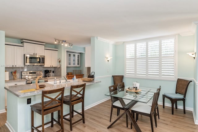 kitchen with white cabinets, backsplash, a kitchen bar, light hardwood / wood-style flooring, and stainless steel appliances